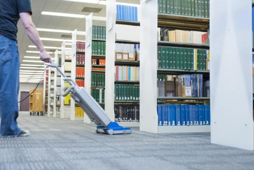 person vacuuming between library book stacks