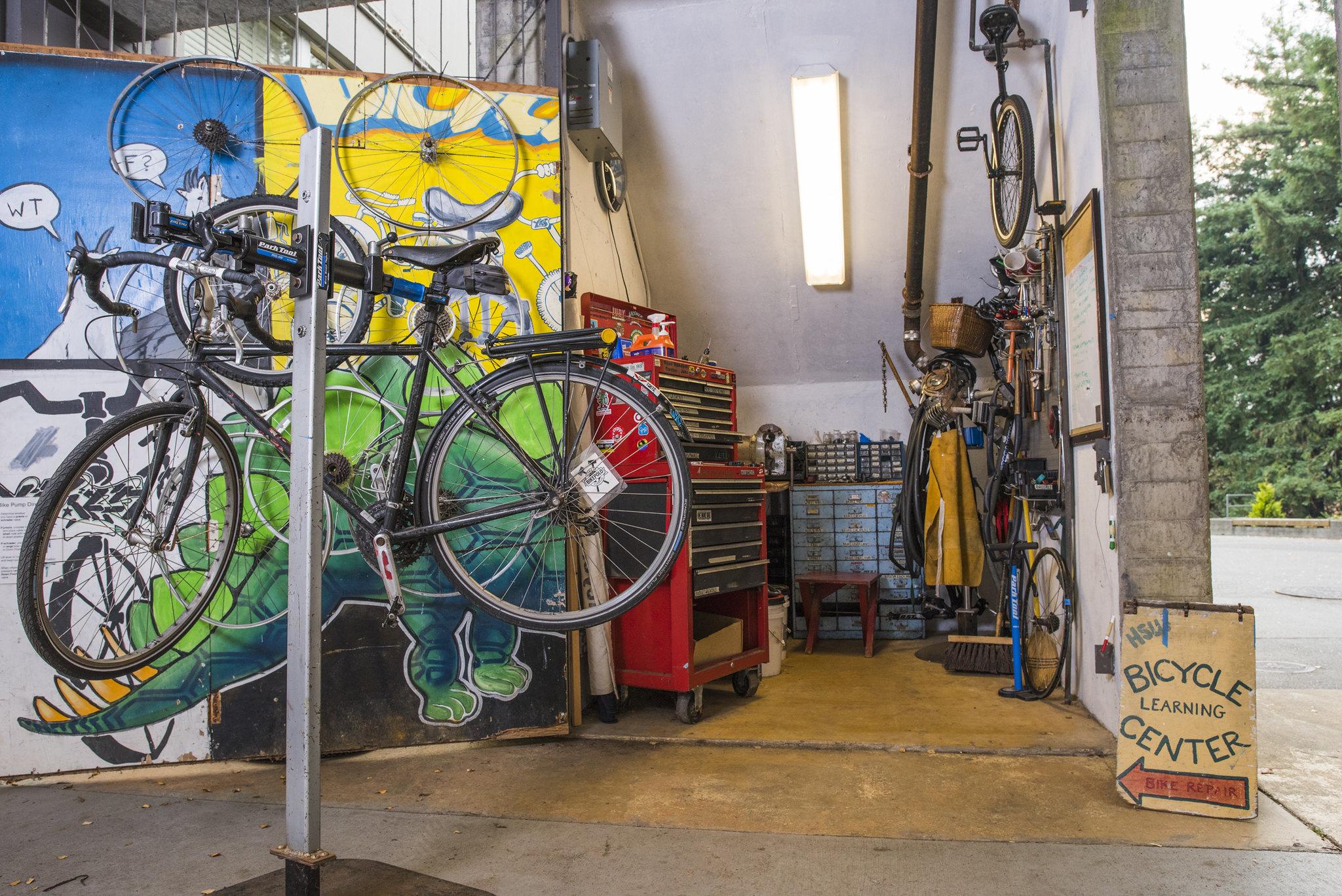 Photo shows a bike held up on a maintenance rack at the Bicycle Learning Center with a colorful mural in the background. 