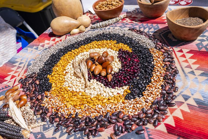 Image shows Indigenous foods laid out in a spiral shape on a table, with acorns in the middle. Photo taken at the 2022 Indigenous Food Fest. 