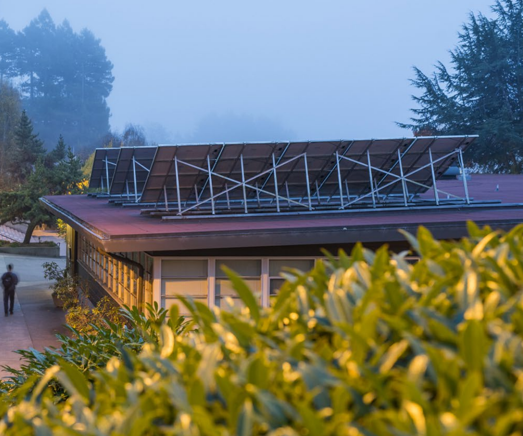 Photo shows the north side/back side of a roof mounted solar array on top of Music A. The lighting is low, photo taken at twilight in foggy conditions. 